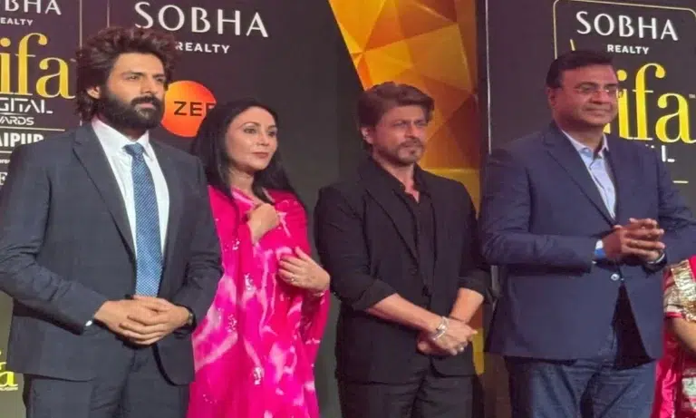 Rajasthan Deputy Chief Minister Diya Kumari, Bollywood stars Kartik Aaryan and Shah Rukh Khan posing together at a press event for IIFA 2025 in Rajasthan, with Jaipur’s iconic pink architecture in the background, celebrating the silver jubilee of the awards.